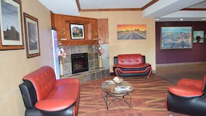 A lobby with a fireplace, red leather sofas, a glass coffee table, and framed artwork on the walls.