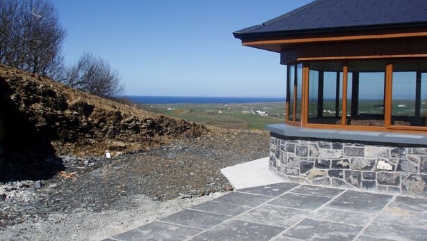 A stone patio leading to a building with large windows and a view of the sea.