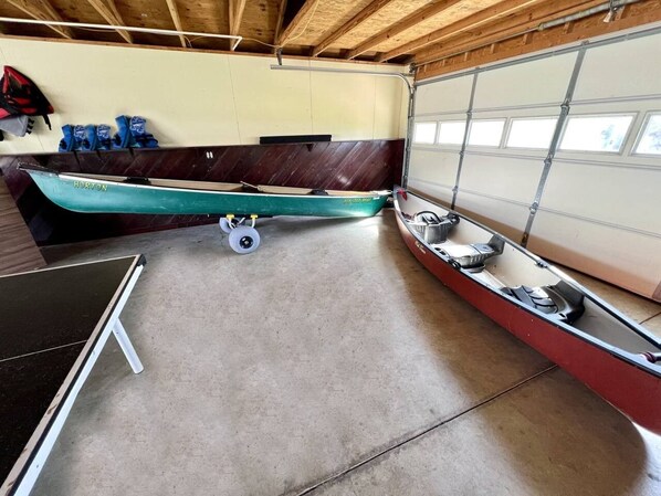 A garage with two canoes, a ping pong table, and a red boat.
