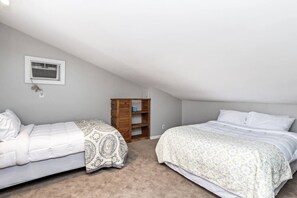 Un dormitorio con dos camas, una estantería de madera y una ventana con unidad de aire acondicionado.