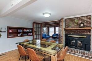 Un comedor con mesa y sillas de vidrio, una chimenea y una estantería llena de libros.