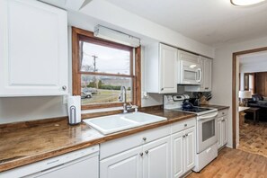 A kitchen with white cabinets, a wooden countertop, a sink, a stove, and a microwave.