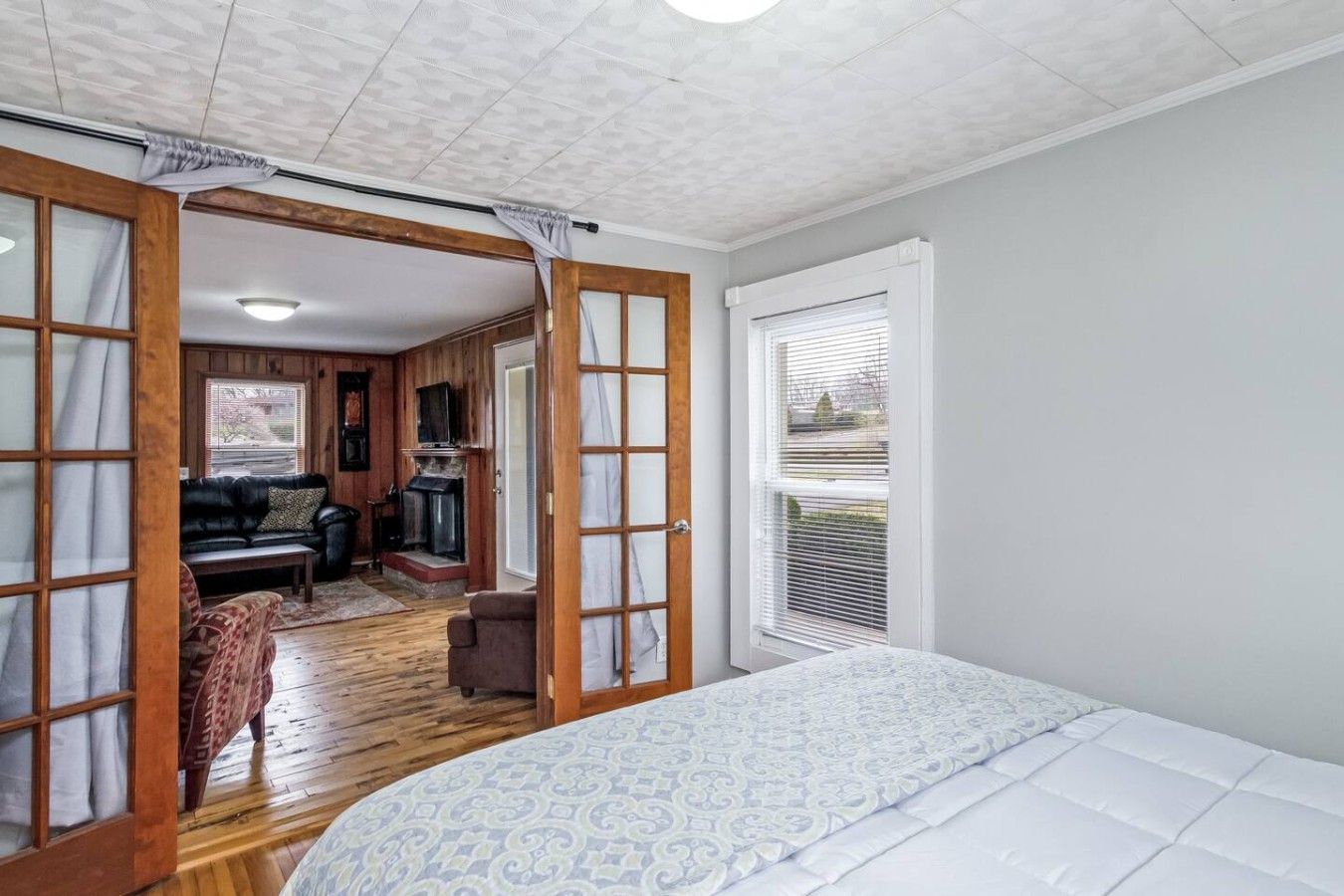A bedroom with a large bed, a wooden floor, a fireplace, and a view of the outdoors.