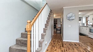 Una escalera con barandillas de madera y peldaños alfombrados que lleva a un pasillo.