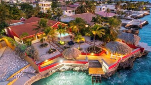Ein Resort mit Pool, umgeben von strohgedeckten Gebäuden, Palmen und Blick auf den Ozean.