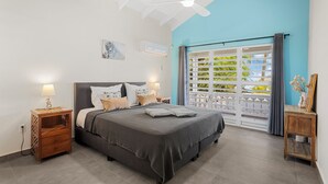 Ein Schlafzimmer mit Bett, Nachttischen, Deckenventilator, Fenster mit Blick und einem Bild an der Wand.