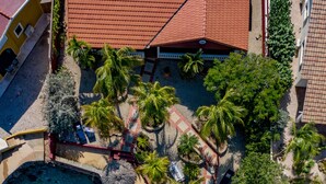 Eine Vogelperspektive zeigt einen Urlaubsort mit einem klaren türkisblauen Pool, Palmen und einem strohgedeckten Gebäude.