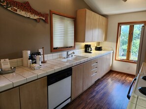 A kitchen with wooden cabinets, a dishwasher, a coffee maker, and a window with a view of greenery. - Snowcreek Resort Vacation Rental 908 (Mammoth Lakes)