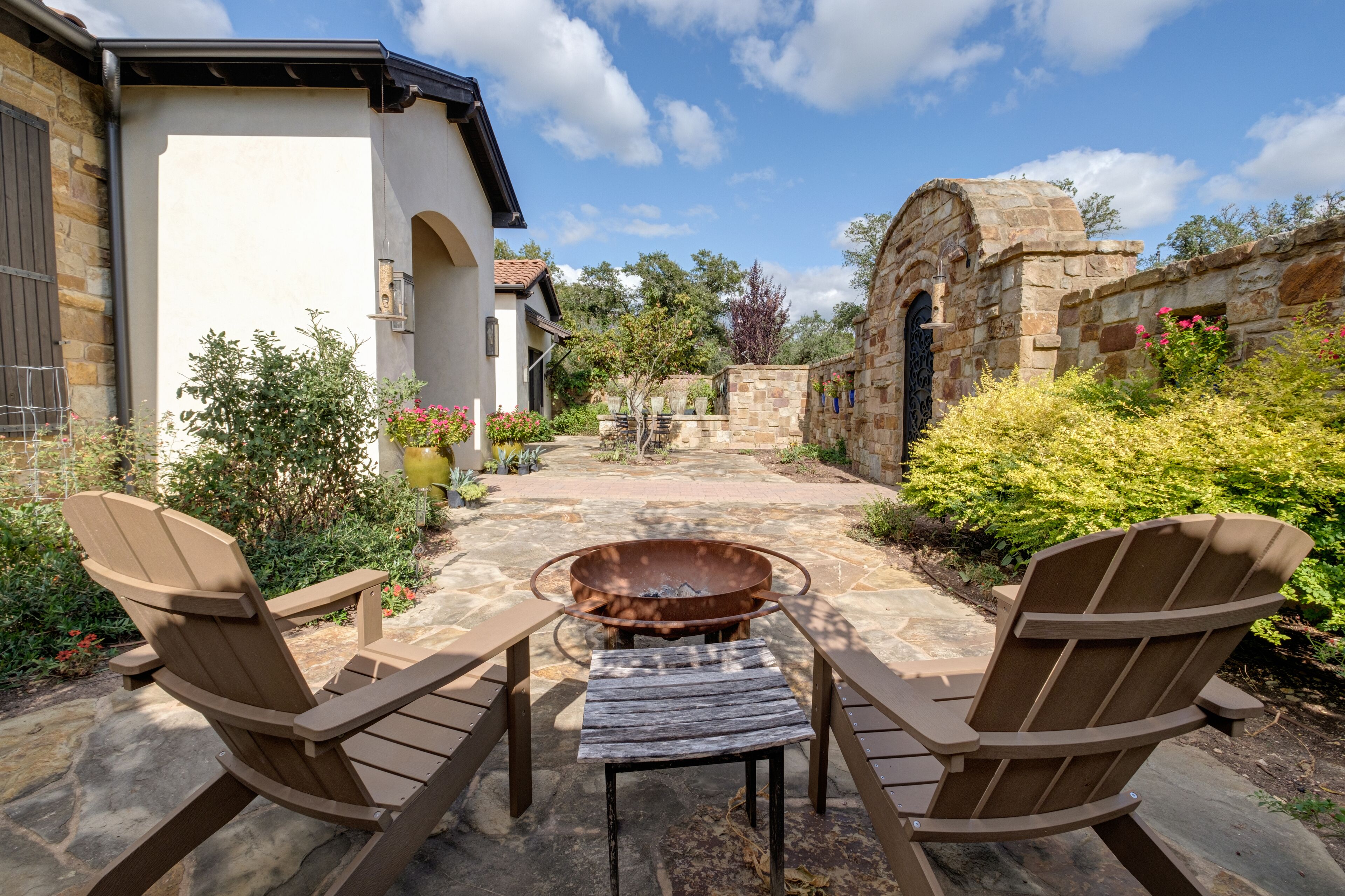 Eine Terrasse mit Adirondack-Stühlen, einer Feuerstelle und einem gepflasterten Weg zu einem Steingewölbe.