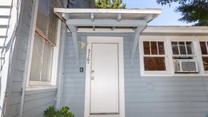 Una casa con puerta blanca, un pequeño porche y una ventana con equipo de aire acondicionado.