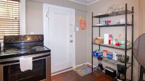 Cocina pequeña con estufa, repisas con vajilla y una puerta.