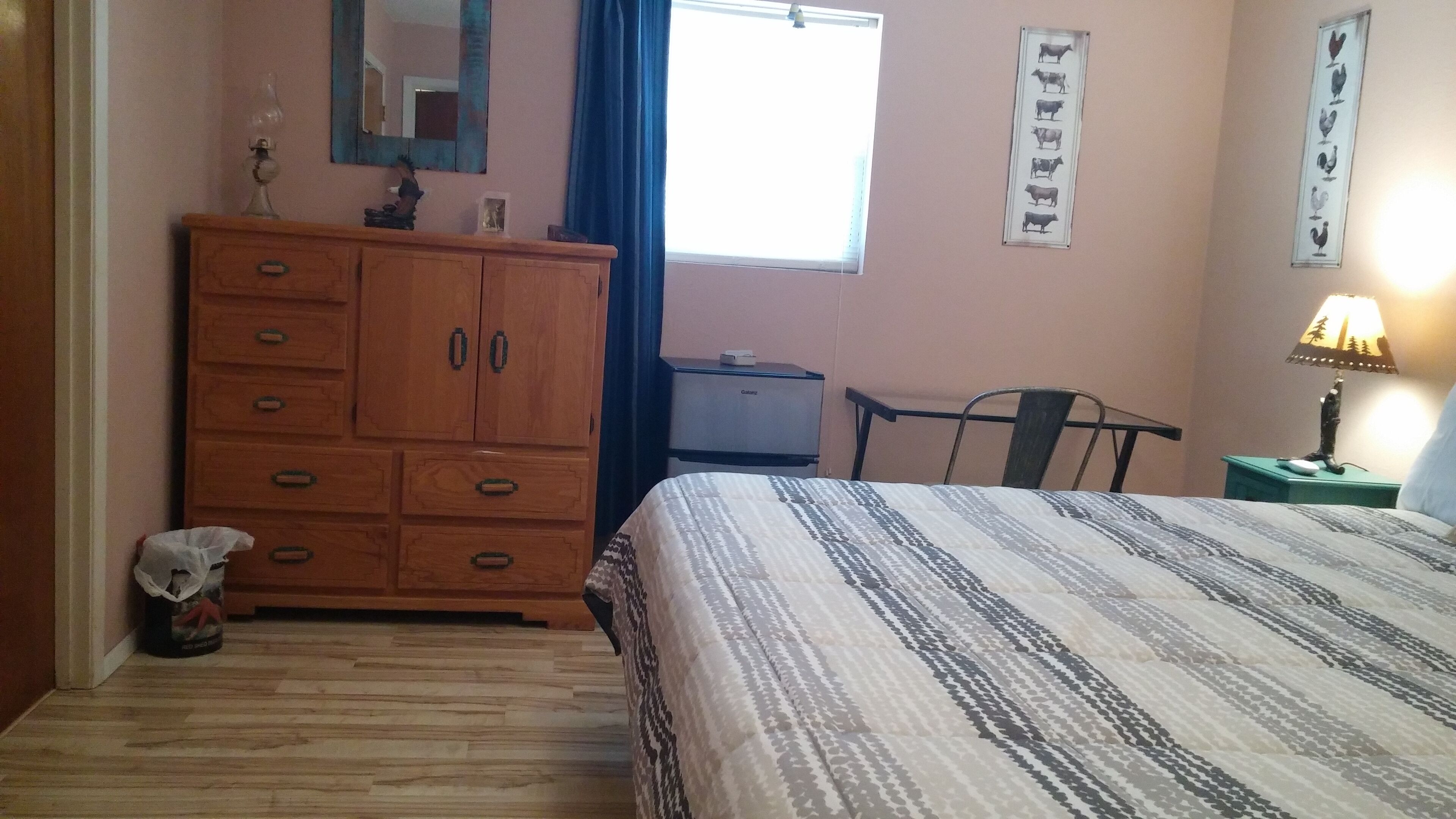 Una camera da letto con un letto, una cassettiera in legno, uno specchio, una finestra e una parete con un quadro incorniciato.