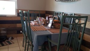Een eethoek met een tafel voor vier personen, omringd door groene stoelen. Op de tafel staan verschillende gerechten en toevoegingen.
