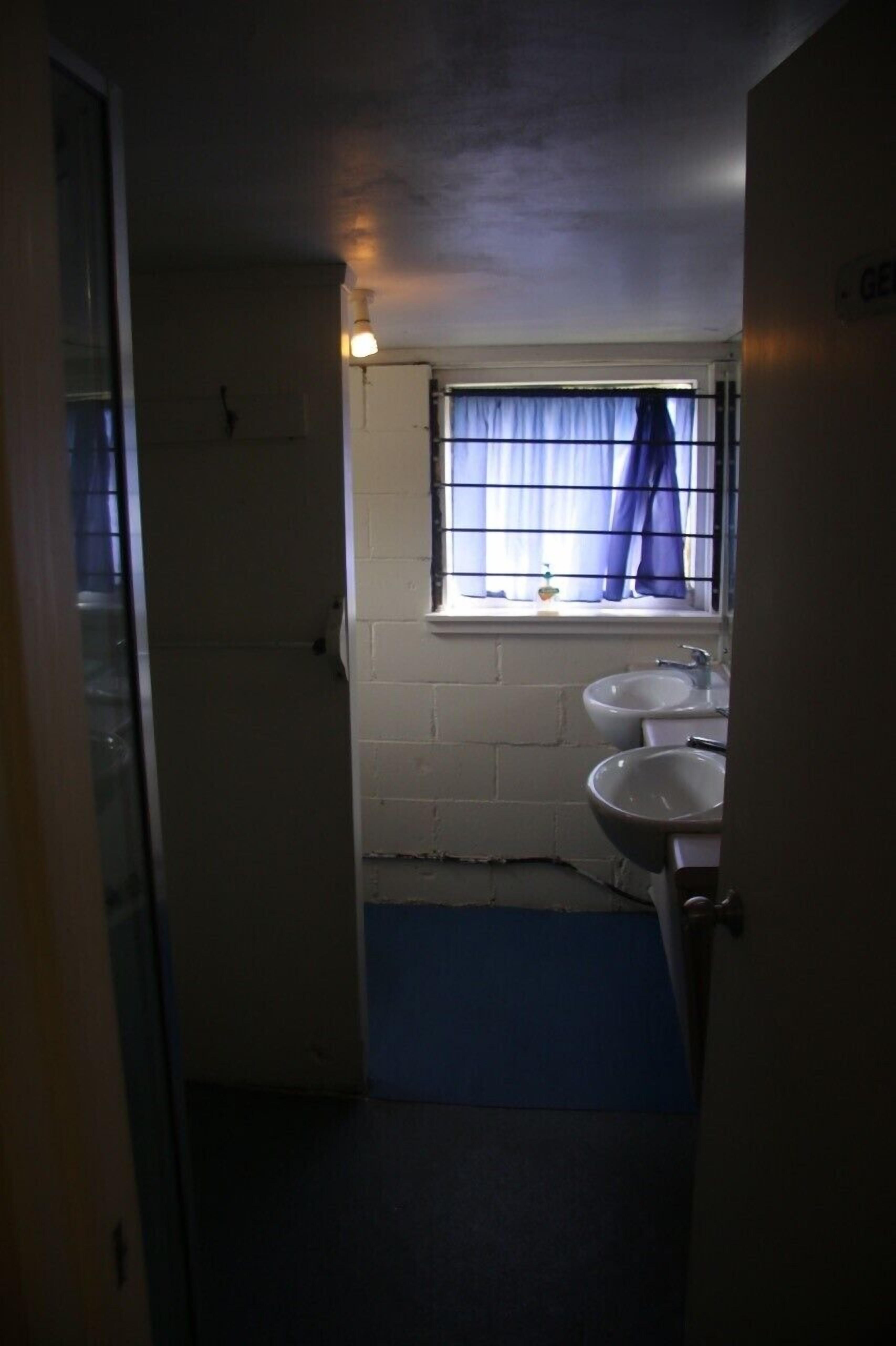 A small bathroom with two sinks, a window with blue curtains, and a blue mat on the floor.