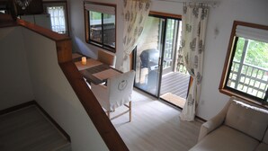 Ein großzügiger Wohnbereich mit einer Holztreppe, einem Esstisch mit Stühlen, einer Couch und einer Glastür zum Außenbereich.