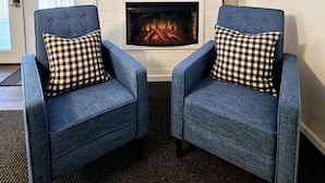 A room with two blue armchairs with checkered pillows, a flat-screen TV above a fireplace, and a door with a window to the left.