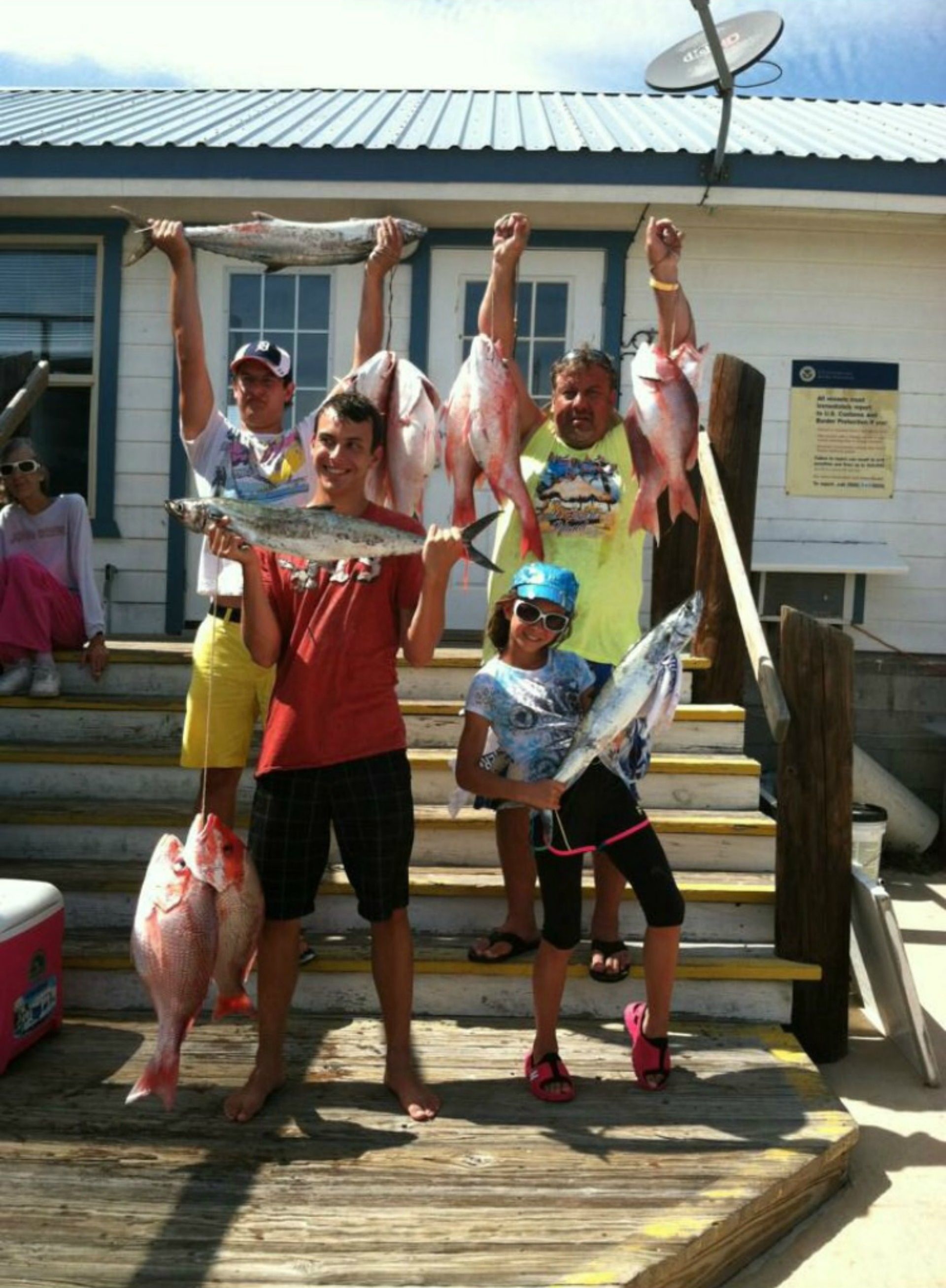A group of people holding fish on a dock with a building in the background.