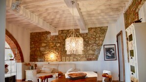Ein gemütliches Wohnzimmer mit Steinwand, Holzbalkendecke, einer Chandelier, einem Sofa, einem Couchtisch und einem Kamin.