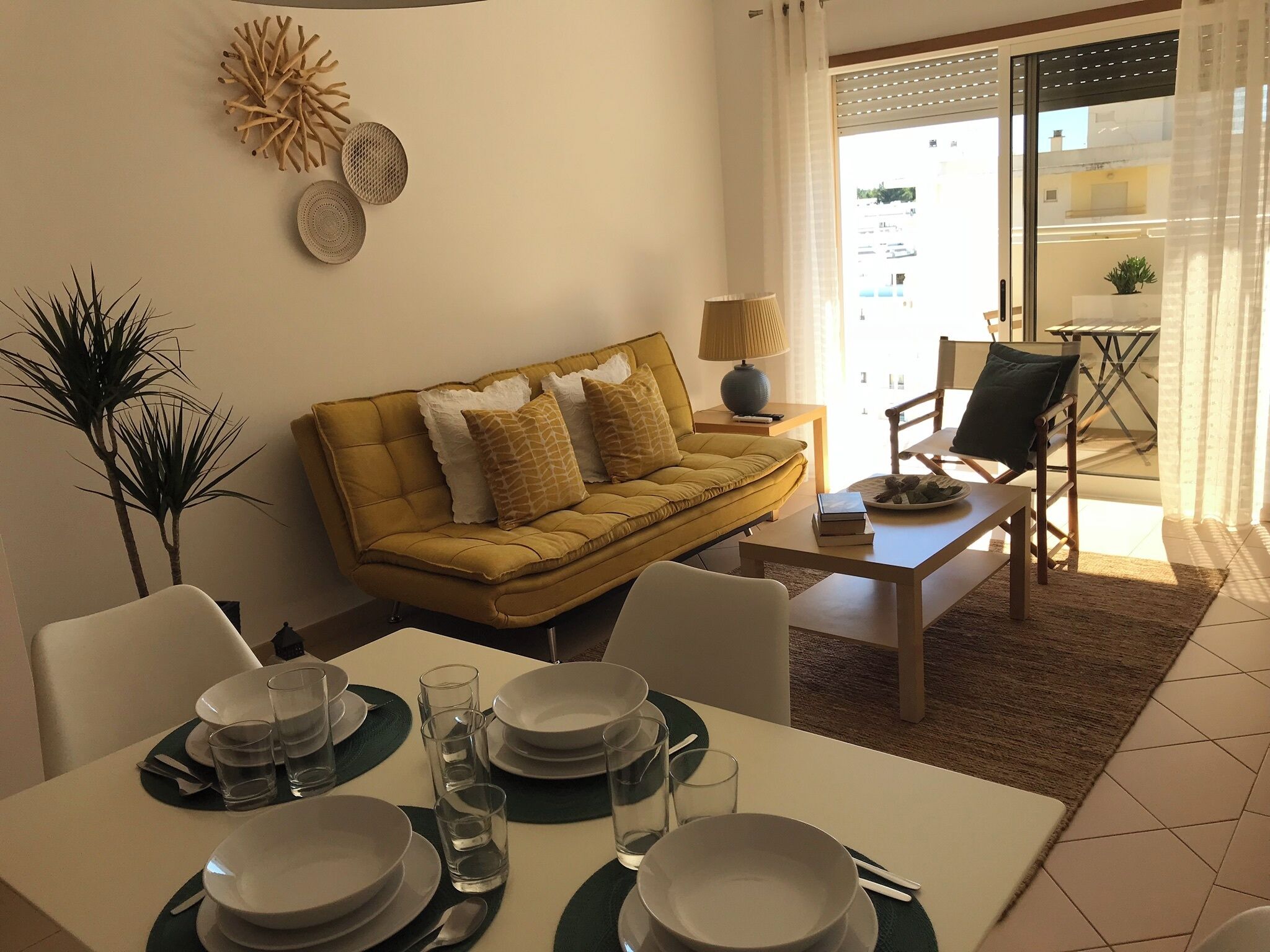 Un salon avec un canapé jaune, une table à manger dressée avec des assiettes et des verres, et une table basse.