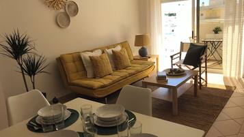 Un salon avec un canapé jaune, une table à manger dressée avec des assiettes et des verres, et une table basse.