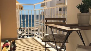 A balcony with a view of the sea, a white railing, a table with a cushion, and a potted plant. - Casa Yeti - Beach House (Armação de Pêra)