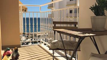 Un balcon avec vue sur la mer, une balustrade blanche, une table avec un coussin et une plante en pot.