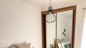 A bedroom with a wooden bed frame, white bedding, a bedside table with a lamp, a tray with tea set, and a large mirror. - Casa Yeti - Beach House (Armação de Pêra)