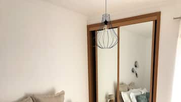 Une chambre avec un lit en bois, du linge de lit blanc, une table de chevet avec une lampe, un plateau avec un service à thé et un grand miroir.