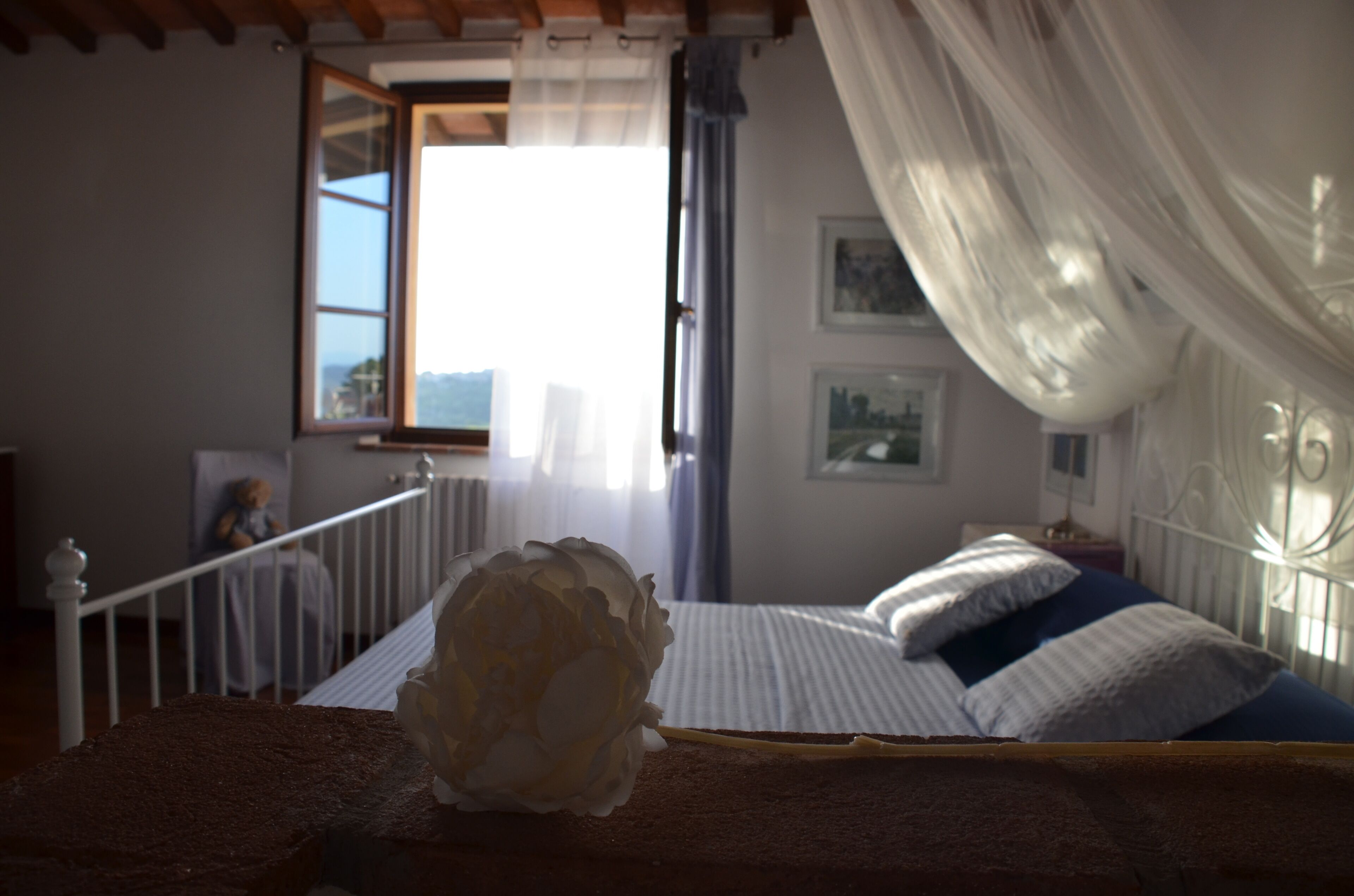 A bedroom with a bed, a window with curtains, a view of the outside, and a decorative object on the bed.