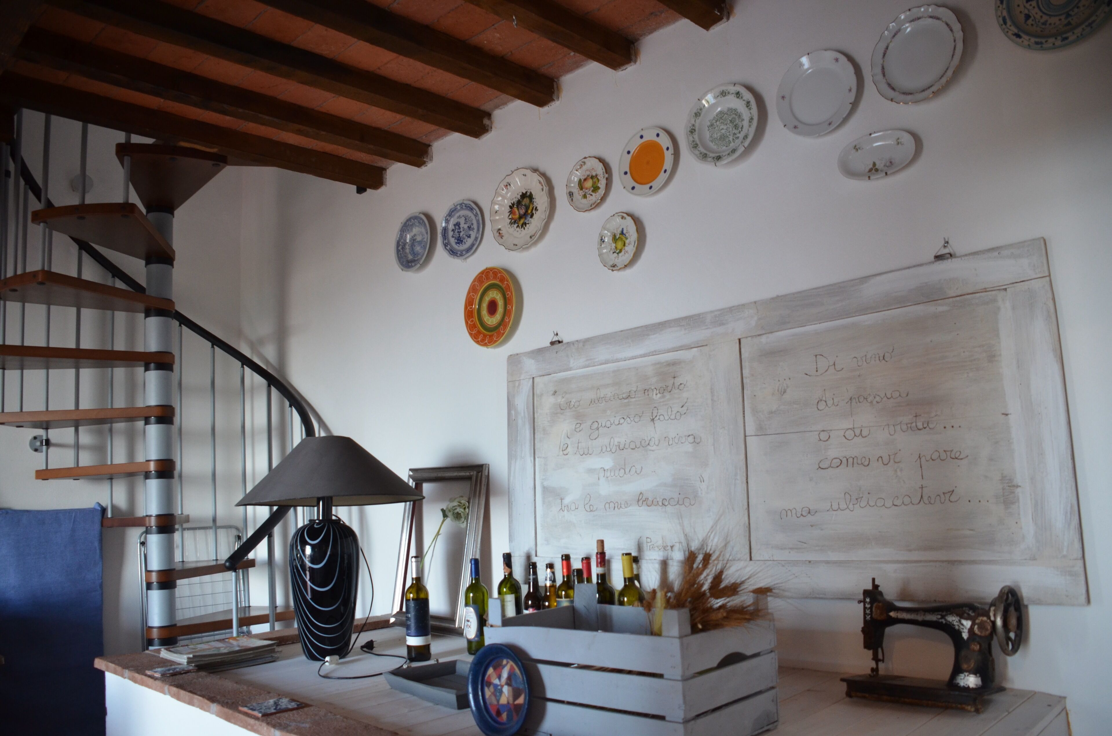 A room with a spiral staircase, a whiteboard with handwritten notes, a collection of wine bottles, and a vintage sewing machine.