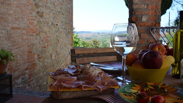 Une table avec un verre de vin blanc, un saladier de fruits et une assiette de charcuteries.