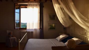 Une chambre à coucher comprenant un lit, une table de chevet, une chaise, une fenêtre avec des rideaux et une vue sur l’extérieur.