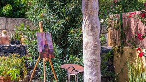 A garden with a palm tree, an easel with a painting, and a small table.