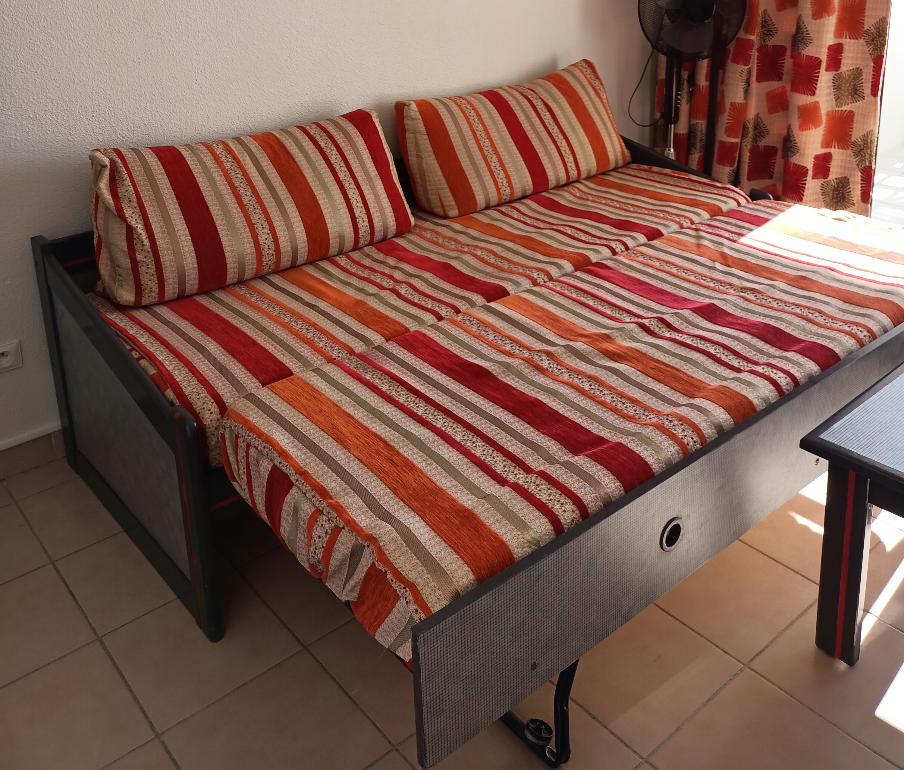 A sofa bed with striped bedding, a dark frame, and a tiled floor.