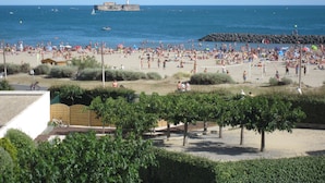 A beach with a rocky breakwater, a lighthouse, and a sandy area with people and umbrellas. - 1st line, sea view, pool and Fort Brescou   (CAP D'AGDE)