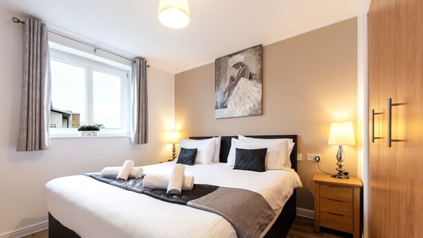 Una habitación de hotel con una cama grande, mesitas de noche, un armario de madera, un cuadro en la pared y una ventana con cortinas.