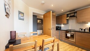 Una cocina moderna con armarios de madera, horno empotrado y una zona de comedor con mesa y sillas de madera.