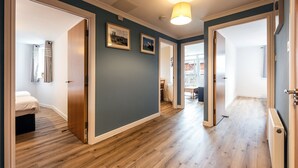 Un pasillo con piso de madera, una lámpara en el techo y puertas que dan a diferentes habitaciones.