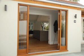 A modern house with a sliding glass door leading to a kitchen with wooden flooring and a dining area visible through the door.