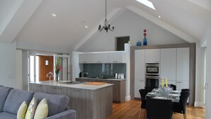 A modern kitchen with a central island, a dining area with a table set for six, and a grey sofa with cushions. - Open Plan Holiday Cottage Within Walking Distance Of Westbourne And Beach (Poole)