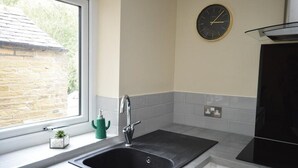A kitchen with a black sink, a green plant, a clock on the wall, and a window overlooking a stone building. - Boutique style centrally located terrace, award winning Skipton Yorkshire Dales (Skipton)