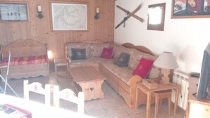 Un salon chaleureux avec un canapé en bois, une table basse en bois et une petite table en bois. Un téléviseur est fixé au mur et un tableau encadré est accroché au-dessus du canapé.