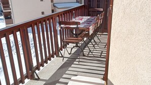 Un balcon avec une table et des chaises, une chaise en plastique blanche, et une vue sur des bâtiments en arrière-plan.