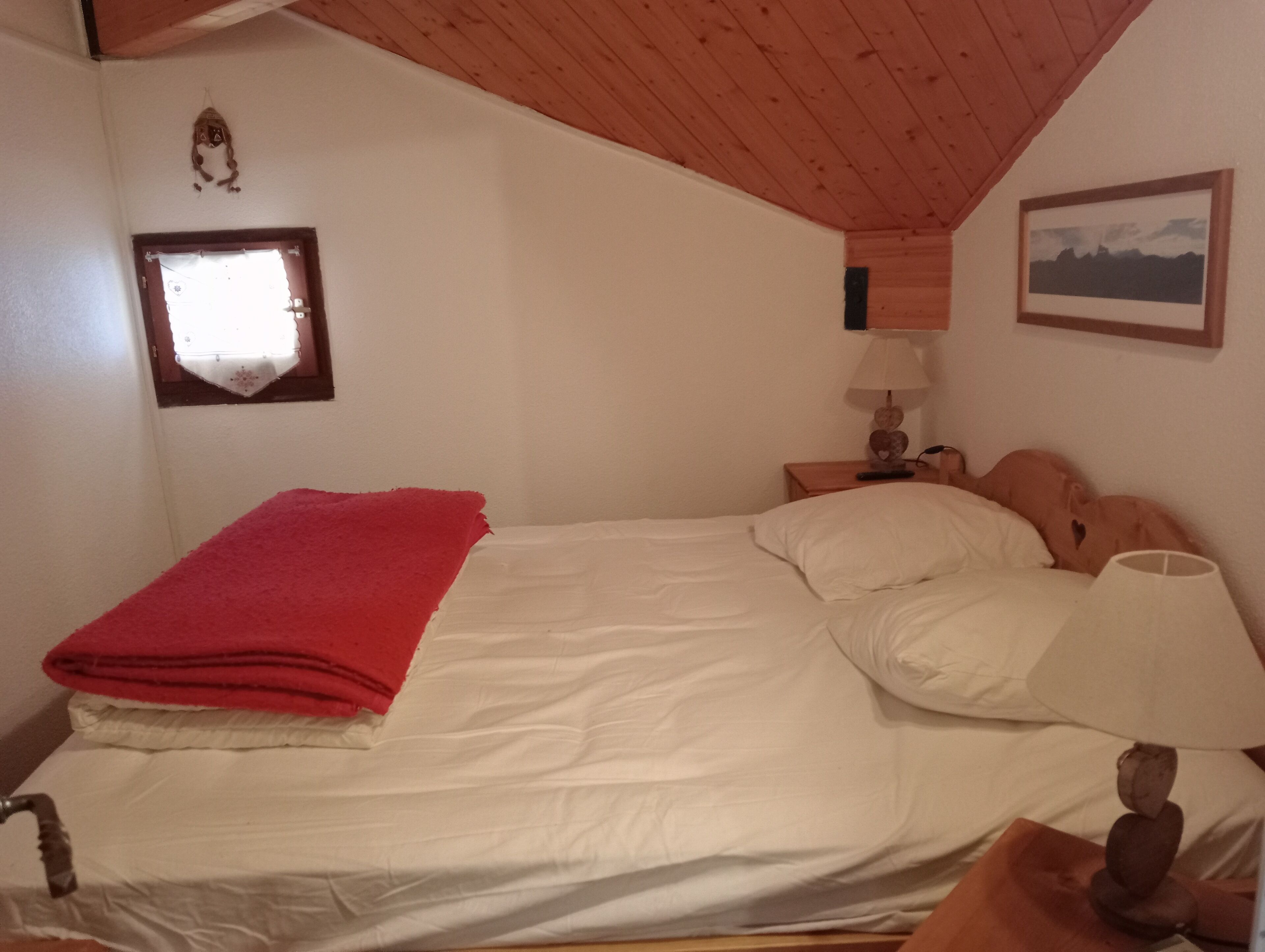 Une chambre à coucher comprenant un lit, une table de chevet, une lampe, une fenêtre et un tableau accroché au mur.