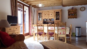 Une pièce chaleureuse avec une table à manger en bois, des chaises, un canapé, un téléviseur et un coin cuisine équipé de placards et d’une horloge.