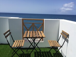A small outdoor seating area with a wooden table and two chairs, overlooking a body of water. - La Lajita Ocean View (La Lajita)