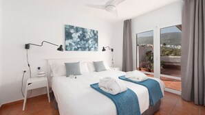 Ein Hotelzimmer mit einem großen Bett, zwei Nachttischen, einem Deckenventilator, Blick ins Freie und einem blauen Kunstwerk an der Wand.