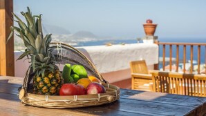 Ein Korbkorb mit Früchten wie Ananas, Apfel, Tomate und grüner Paprika auf einem Holztisch.