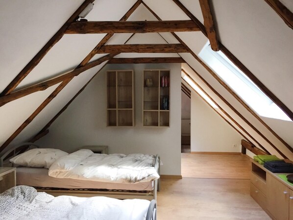 A small attic bedroom with a sloped ceiling, wooden beams, a bunk bed, a small desk, and a window. - Vacation apartment "Kaminzimmer" in the 2-stall country house in the Rhodo garden. (Westerstede)