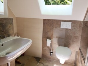 Un baño con lavamanos, inodoro y una ventana sobre el inodoro.